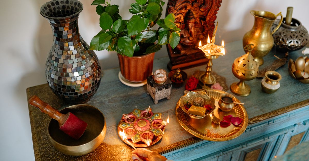 Pequeño altar doméstico con lamparita de aceite, flores y recipientes de cobre sobre una mesa de madera